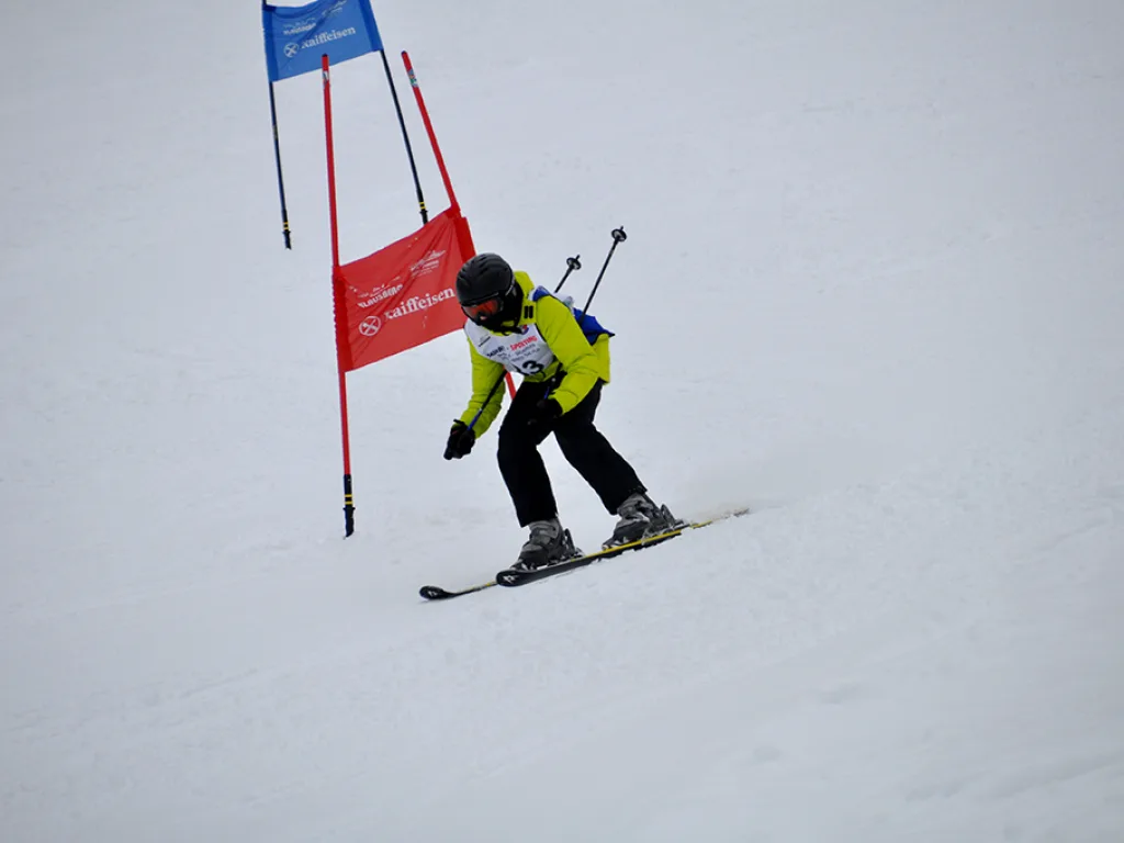 Snowboarder in gelber Jacke umfährt ein rotes Tor.